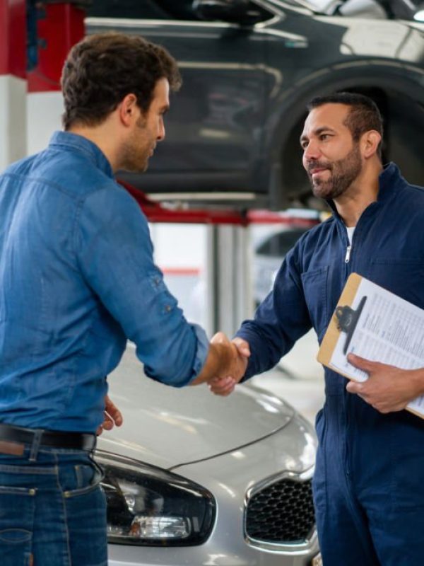 Latin American man greeting a mechanic with a handshake while picking up his car at an auto repair shop